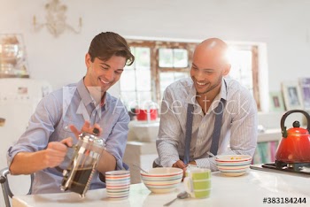 Young male roommates enjoying coffee and cereal in morning kitchen