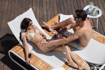 Young man applying sunscreen on girlfriend on sunny lounge chairs
