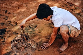 Young man crouching on the beach drizzling sand and making sand castles