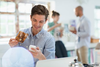 Young man eating toast and checking smart phone in morning kitchen