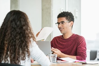 Young Man In Meeting Going Over Reports