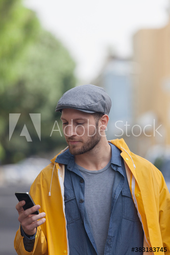 Young man in raincoat using smart phone