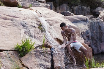 Young man in swim trunks at rocks with waterfall