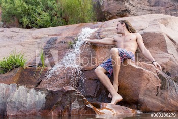 Young man in swim trunks on rock with waterfall