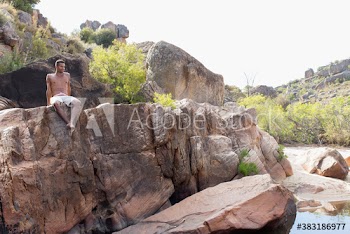 Young man in swim trunks relaxing on sunny rocks