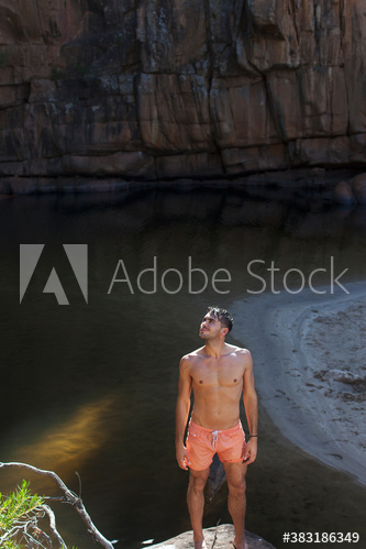 Young man in swim trunks standing on rock above water