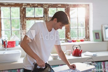 Young man ironing shirt in morning kitchen