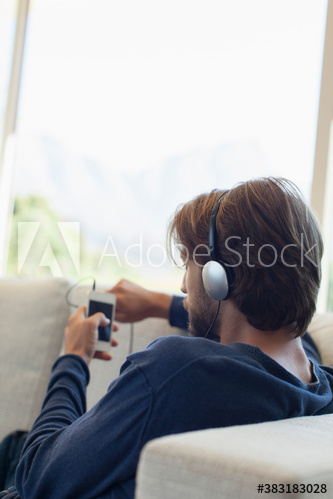 Young man listening to music with headphones and mp3 player on sofa