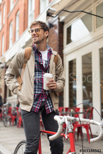 Young man on bicycle drinking coffee on city sidewalk