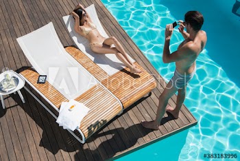 Young man photographing girlfriend sunbathing in sunny lounge chair