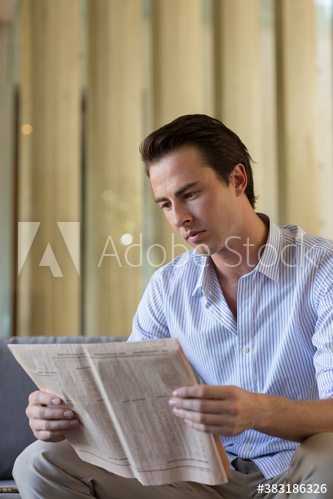 Young man reading newspaper on sofa