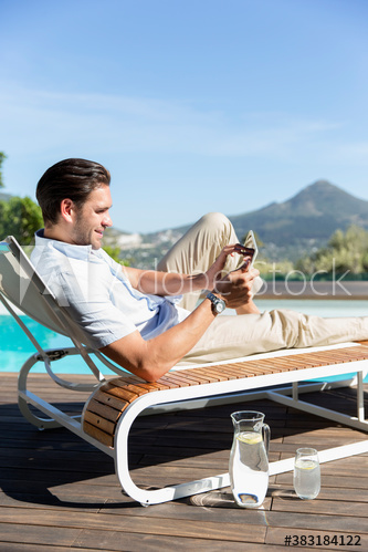 Young man using digital tablet on lounge chair at sunny poolside