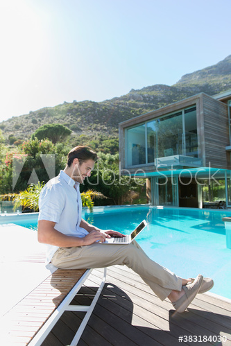 Young man using laptop at sunny luxury poolside