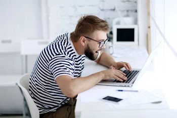 Young man with facial expression sitting at desk with laptop