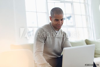 Young man with laptop working from home on sofa