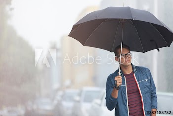 Young man with umbrella on rainy city street