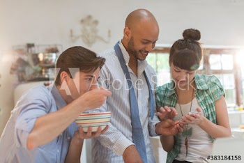 Young roommates eating breakfast and using smart phone in kitchen