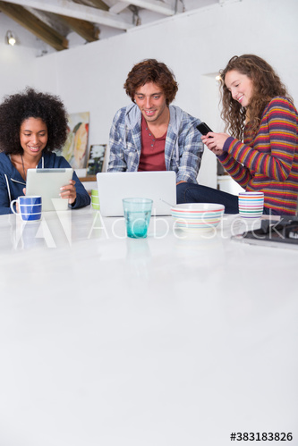 Young roommates using digital tablet laptop and smart phone at table