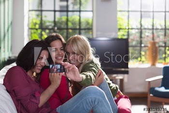 Young woman friends taking selfie with camera on sofa