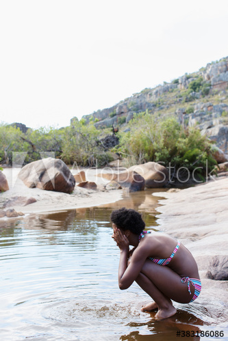 Young woman in bikini splashing water on face at lake