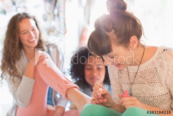 Young woman painting toenails of friend with nail polish