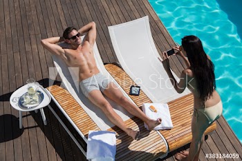 Young woman photographing boyfriend sunbathing on sunny lounge chair
