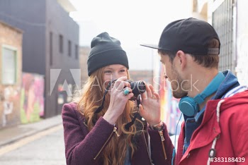 Young woman photographing boyfriend with camera on city street