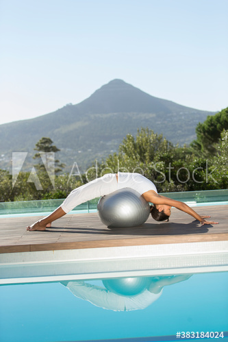 Young woman practicing backbend stretch with fitness ball at poolside