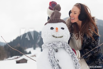 Young woman putting knit hat on snowman in snowy field