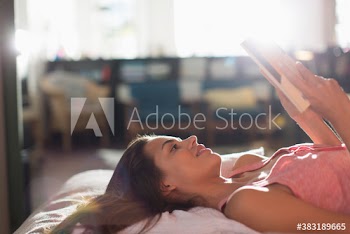 Young woman reading book and relaxing on sunny bed