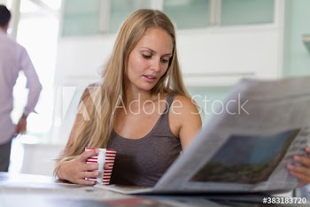 Young woman reading newspaper and drinking coffee