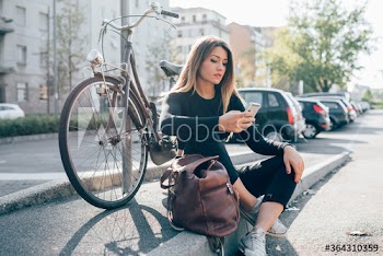 Young woman sitting on sidewalk with bicycle parked in background