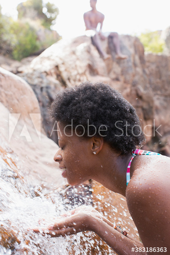 Young woman splashing water on face at waterfall