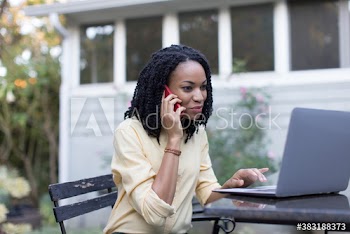 Young woman talking on smart phone at laptop on patio