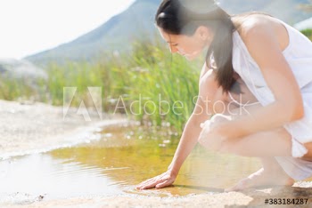 Young woman touching fresh sunny puddle
