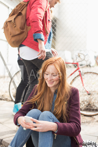 Young woman using smart phone on sunny curb
