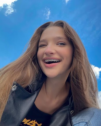 Young woman wearing black leather jacket and denim pants and have braces, pose outside, it's sunny