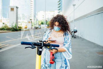Young woman wearing medical mask using smartphone for unlocking electric scooter on street