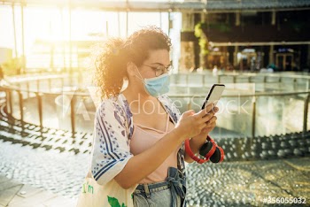 Young woman wearing surgical mask using smartphone outdoors