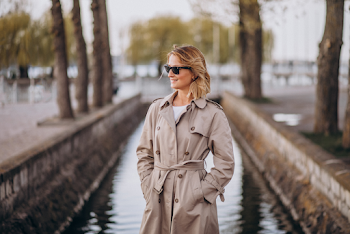 Young woman wearing trench-coat and sunglasses, posing in the city