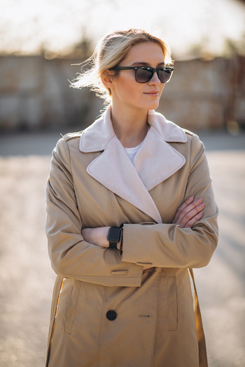 Young woman wearing trench-coat and sunglasses, posing in the city