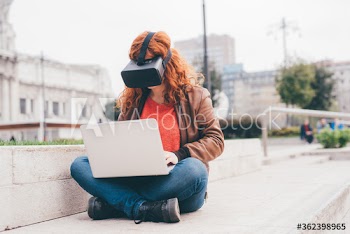 Young woman wearing VR glasses while using laptop on street