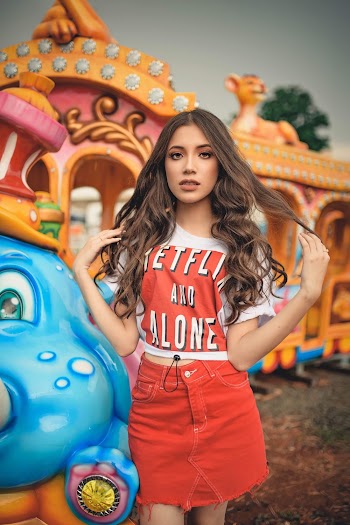 Young Woman With Long Hair In Casual Wear Standing Beside An Amusement Park Train Ride