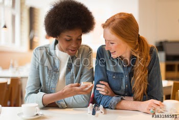 Young women friends using smart phone in cafe