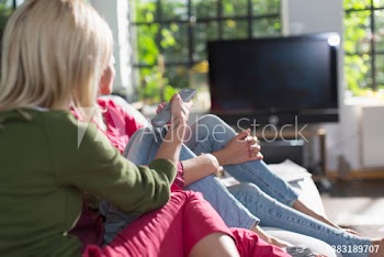 Young women friends watching TV on sofa